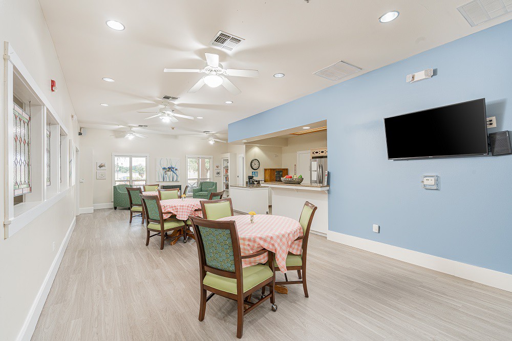 A spacious dining area with tables and chairs, featuring ceiling fans and a television mounted on the wall.
