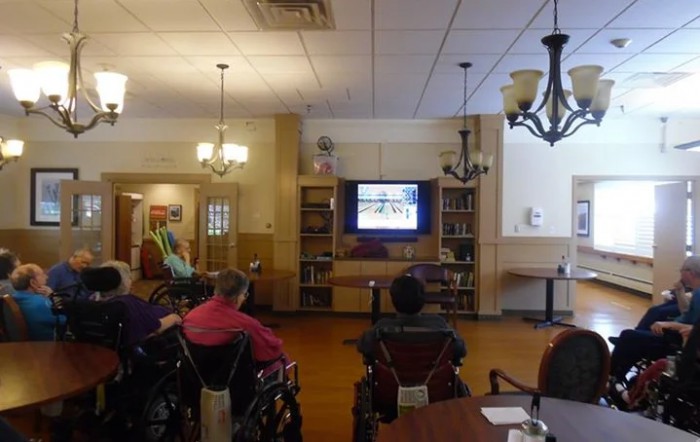 Residents in a nursing home gather to watch television together in a common area.