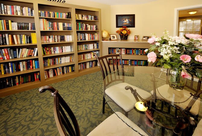 A cozy library room with bookshelves, a glass table, and floral decorations.