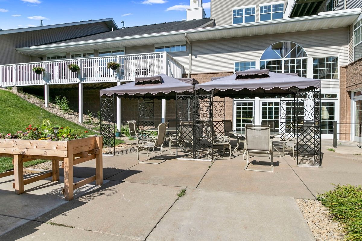 Sunny patio area with outdoor furniture and umbrellas in front of a building.