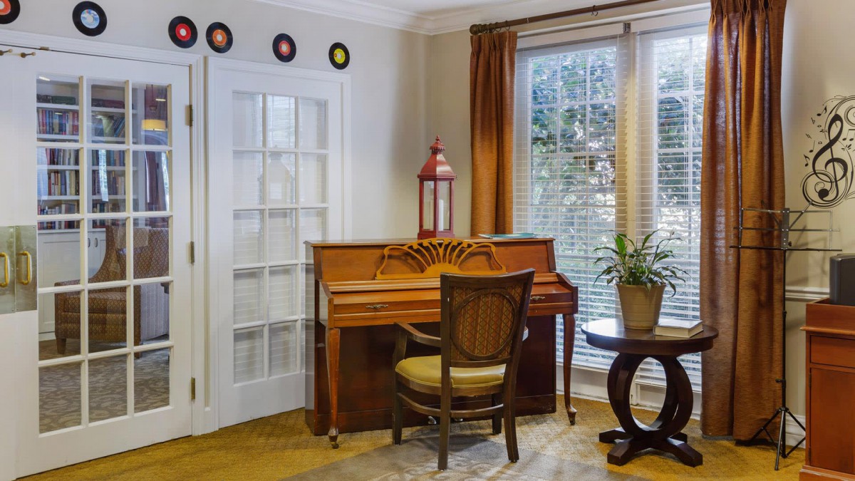 A cozy music room with a piano, chair, and decorative accents by the window.