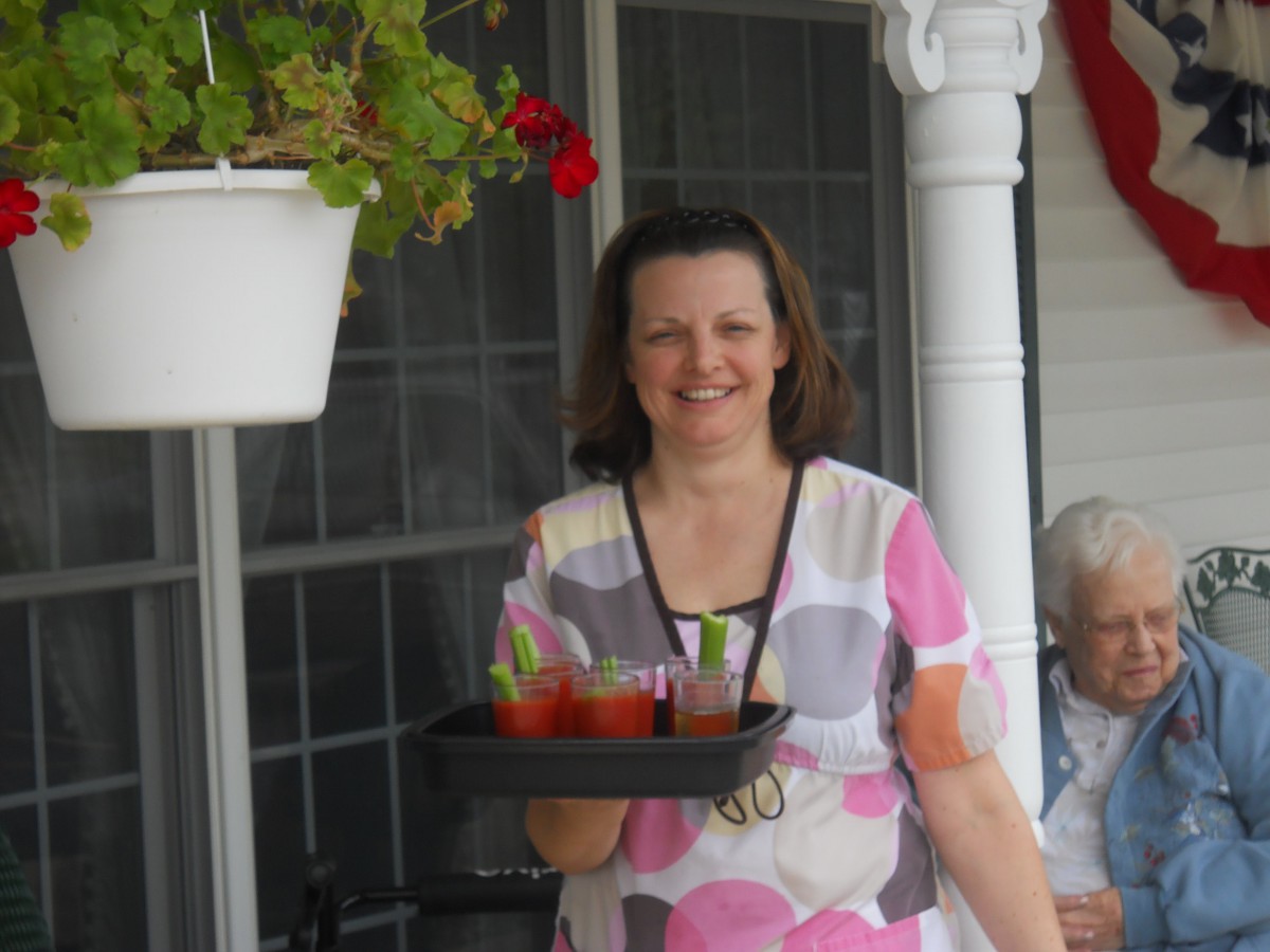 A woman standing on a porch holding a tray of drinks.