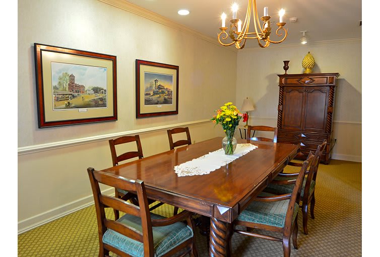 A cozy dining room featuring a wooden table, chairs, and a chandelier, complemented by wall paintings and elegant decor.