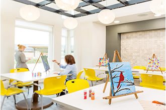 A bright art studio with paintings on easels and a person engaged in painting.