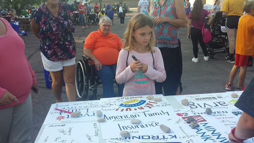 A young girl participating in a community event, engaging with a table of information from American Family Insurance.