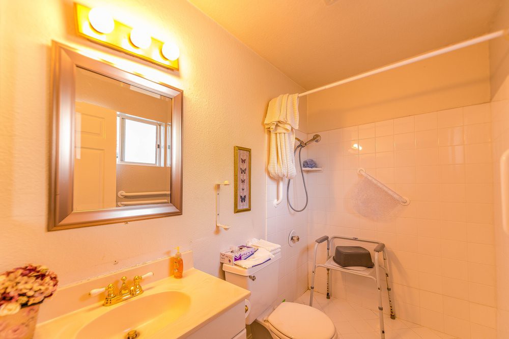 A bright bathroom with a shower, sink, and a shower chair.