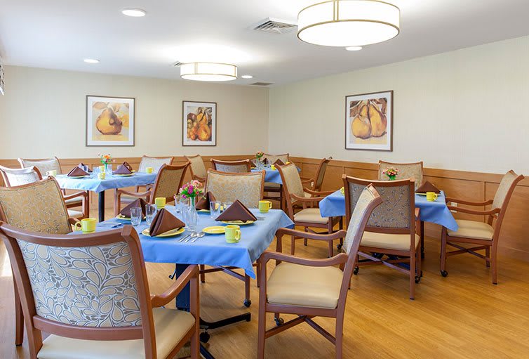 A well-decorated dining room with tables and chairs arranged neatly, featuring ceiling lights and artwork on the walls.