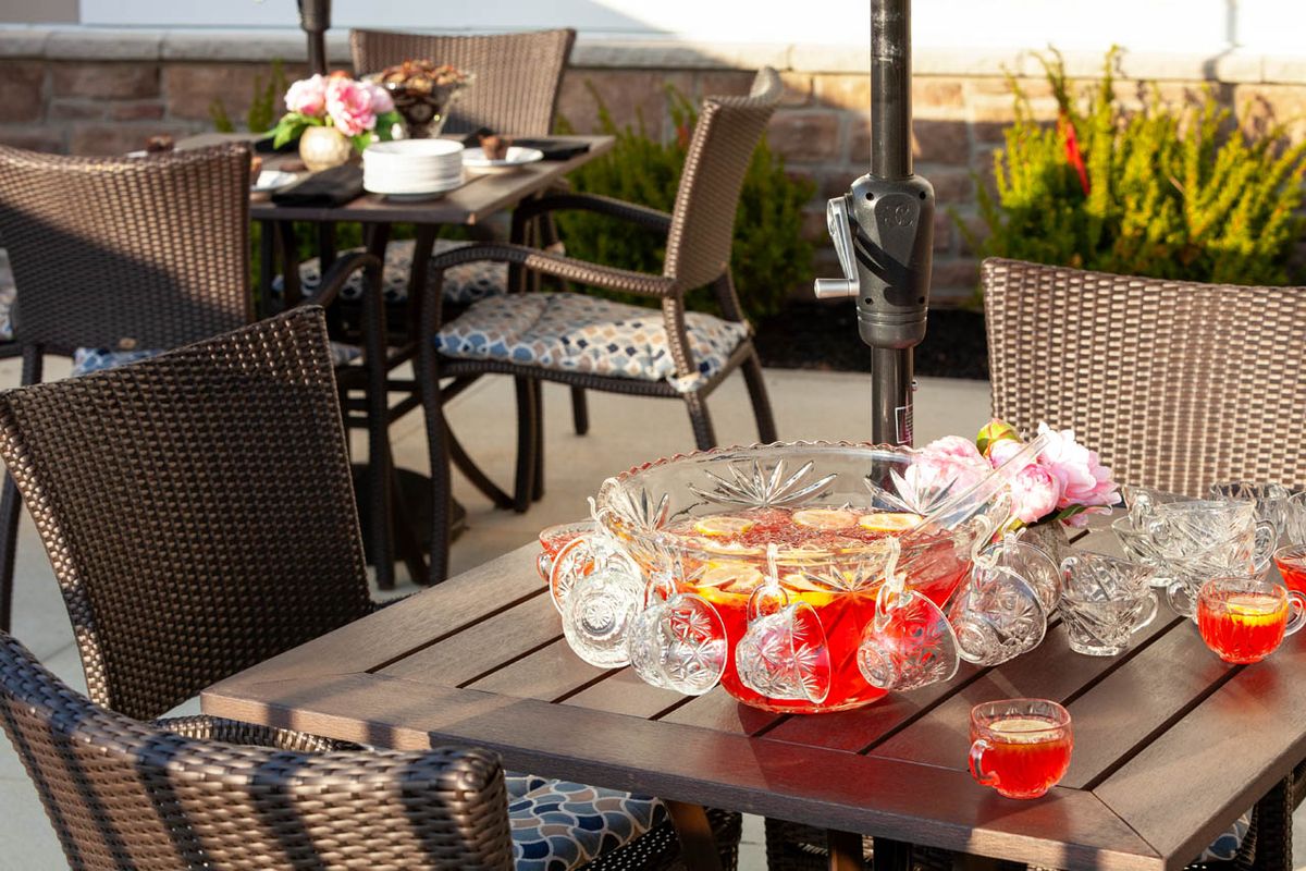 An outdoor patio setup featuring a table with a punch bowl, glasses, and flowers.