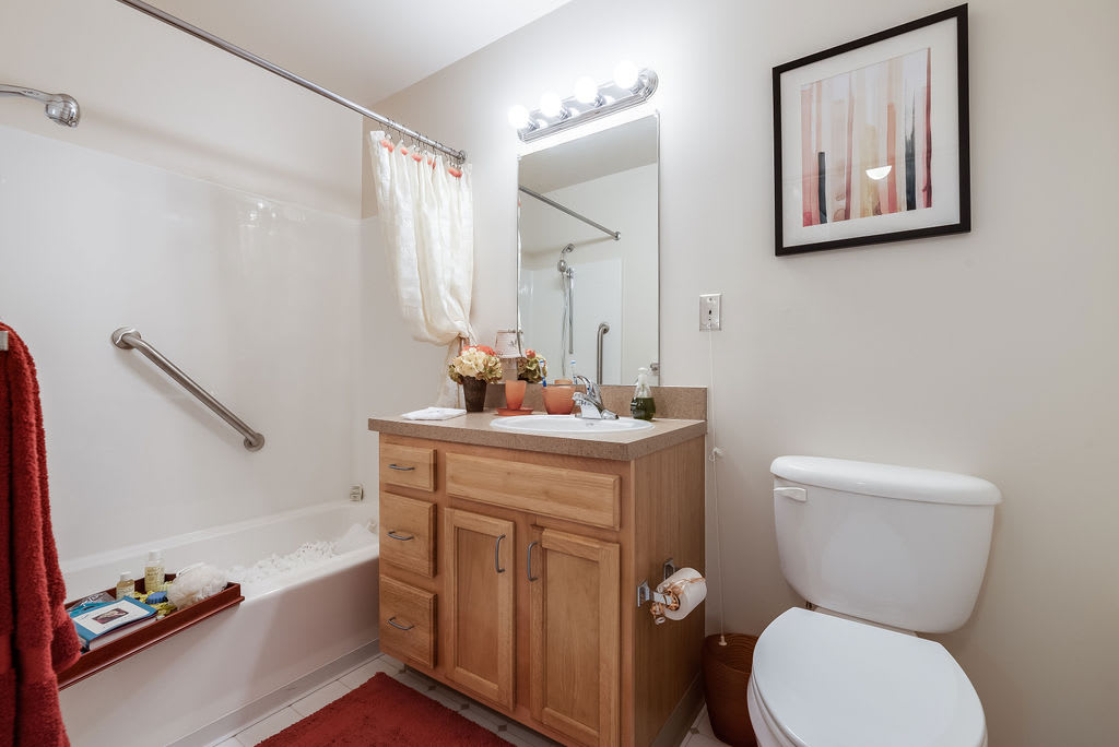 A clean and modern bathroom featuring a wooden vanity, mirror, and white fixtures.