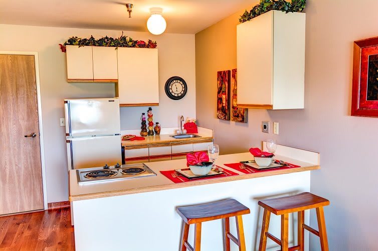 A cozy kitchen with a counter and bar stools, decorated with vibrant accents and warm lighting.