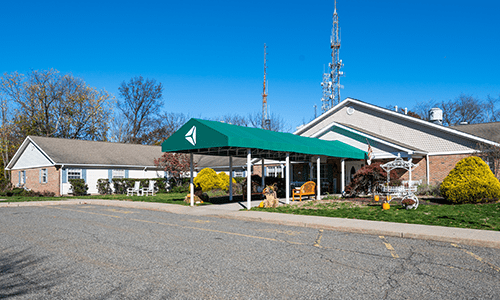 A view of a building with a green awning and an antenna, surrounded by trees under a clear blue sky.