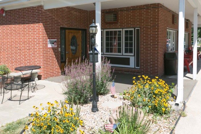 The entrance of a brick building with a garden featuring yellow flowers and a lamp post.