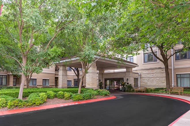 The entrance to a building surrounded by trees and landscaped greenery.