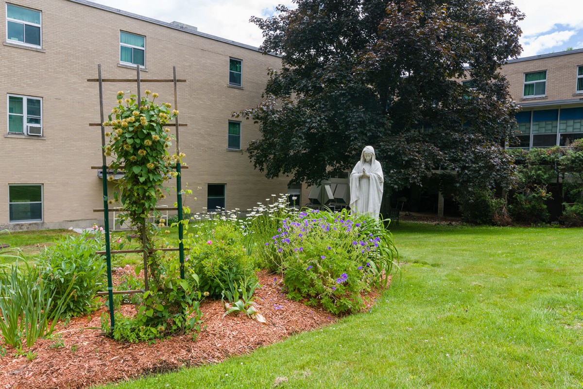 A serene garden with a statue surrounded by greenery and flowers in front of a building.