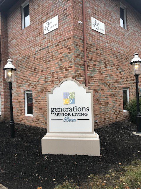 A sign for Generations Senior Living in front of a brick building with lamp posts.