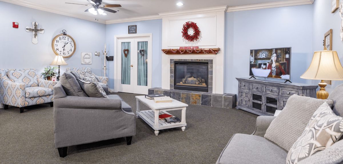 A cozy living room featuring a fireplace adorned with a red wreath, comfortable gray sofas, and a white coffee table.