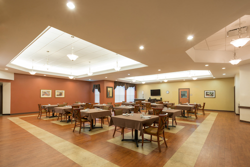 A spacious dining room with neatly arranged tables and chairs, featuring warm lighting and inviting decor.
