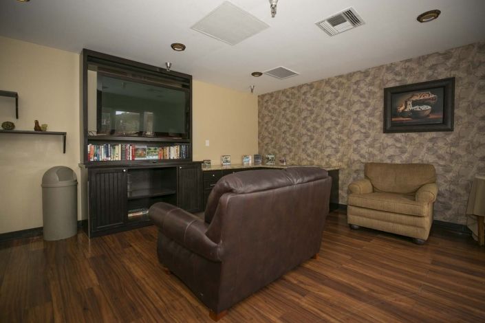 A cozy living room with a brown leather sofa, bookshelf, and patterned wallpaper.