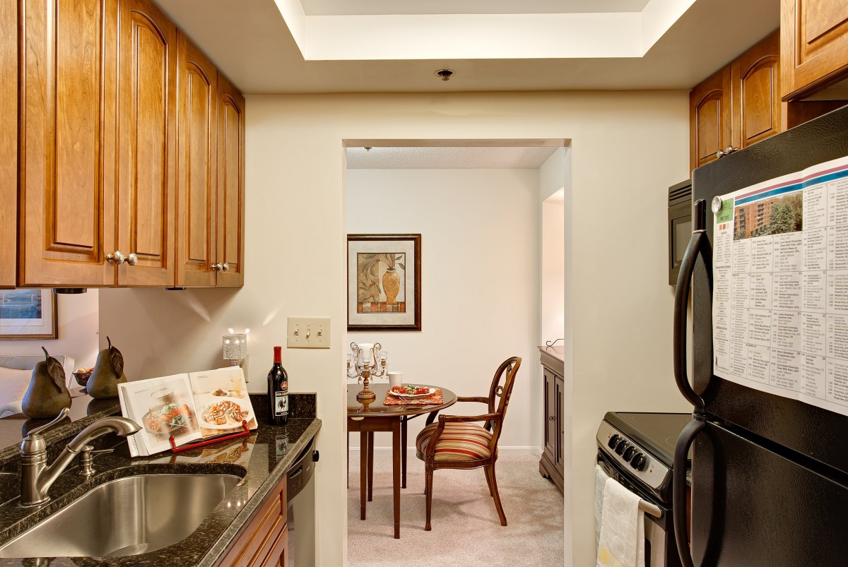 A cozy kitchen with wooden cabinets leading to a dining area featuring a small table and chairs, adorned with artwork on the wall.