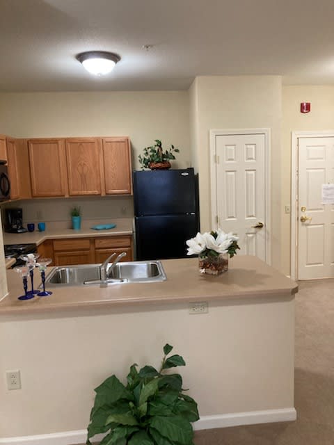 A cozy kitchen with wooden cabinets, a black refrigerator, and a countertop adorned with flowers.