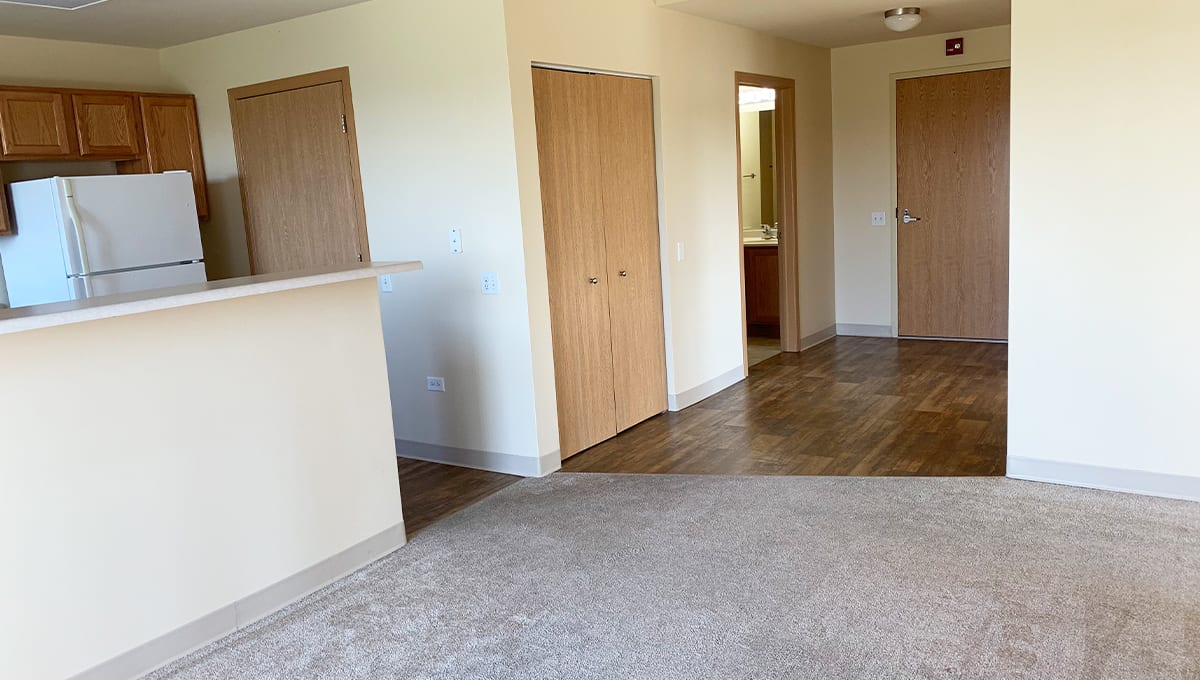 An empty apartment interior with carpet and tile flooring, featuring wooden doors and white walls.