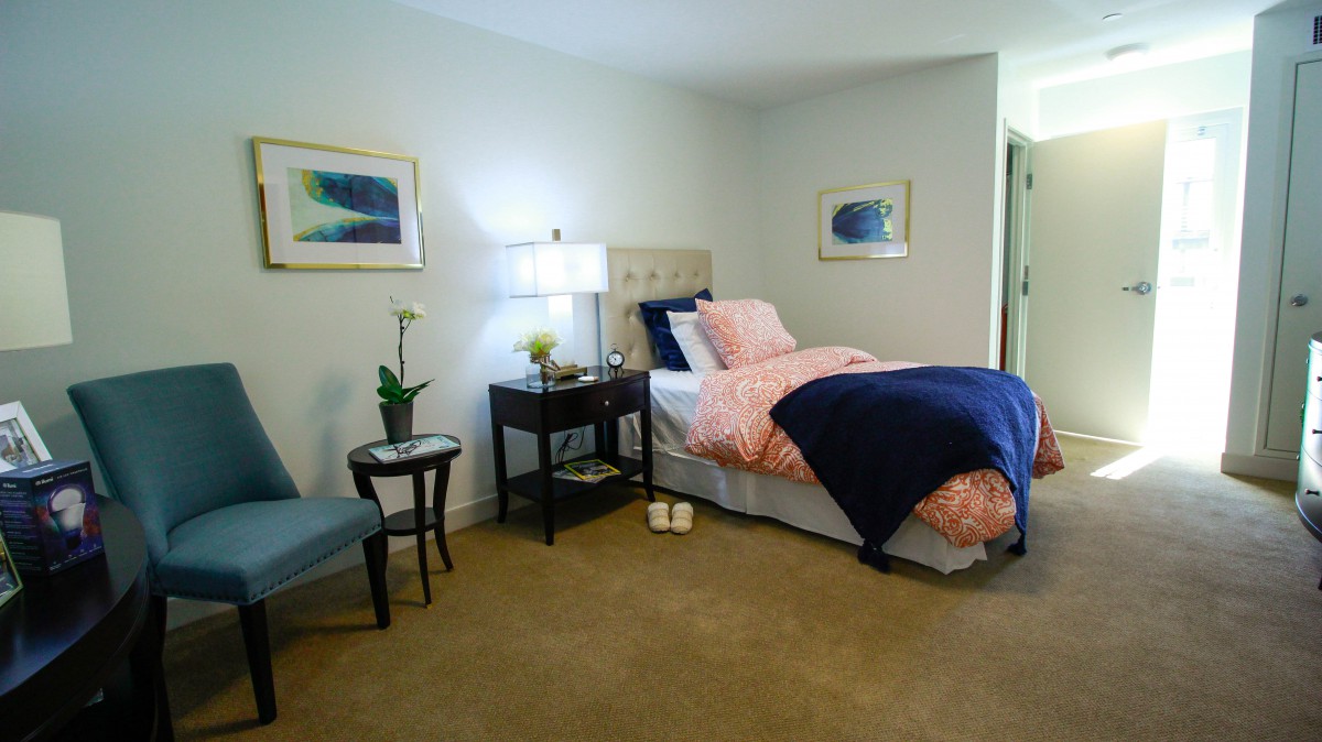 A cozy bedroom with a neatly made bed, side table with a lamp, and framed artwork on the walls.