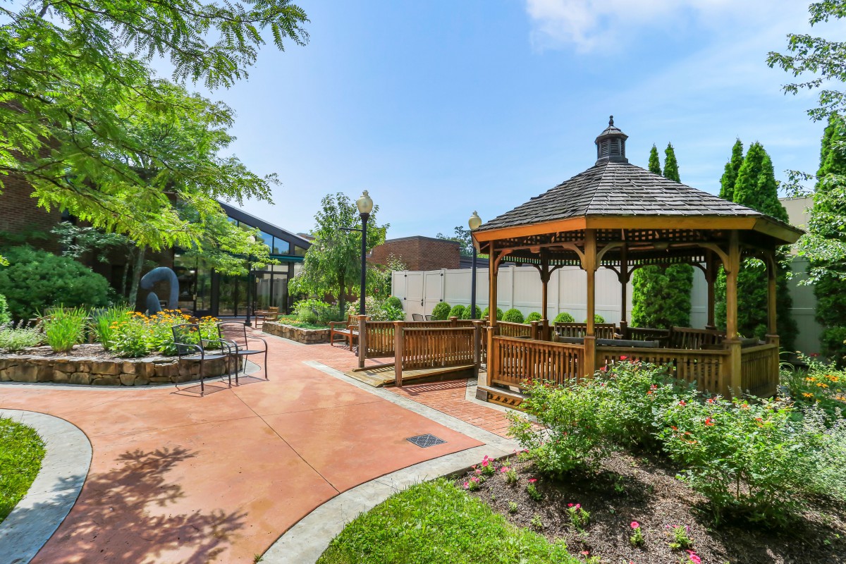 A serene garden featuring a wooden gazebo and winding pathway surrounded by lush greenery.