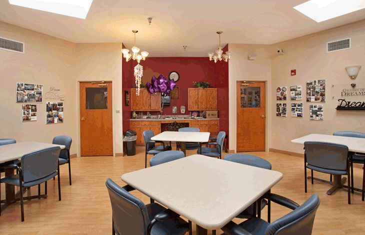 A cozy dining area with tables and chairs, featuring a small kitchenette in the background and decorated walls.