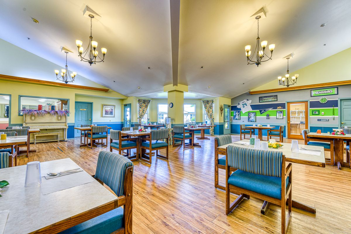A well-lit and inviting dining area with arranged tables and chairs, featuring chandeliers and a wooden floor.