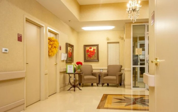 A cozy waiting room with comfortable chairs, a small table, decorative paintings, and a chandelier.