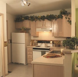 A cozy kitchen with wooden cabinets, a white refrigerator, and decorative greenery above the cupboards.