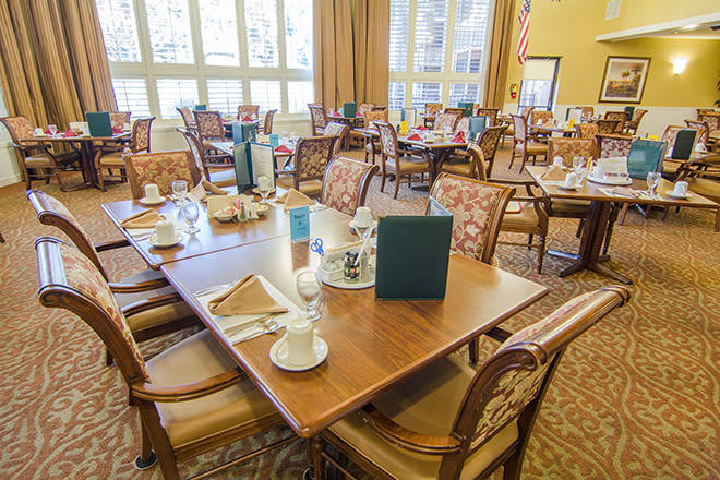 A cozy dining room with multiple tables and chairs, neatly set with menus and tableware.
