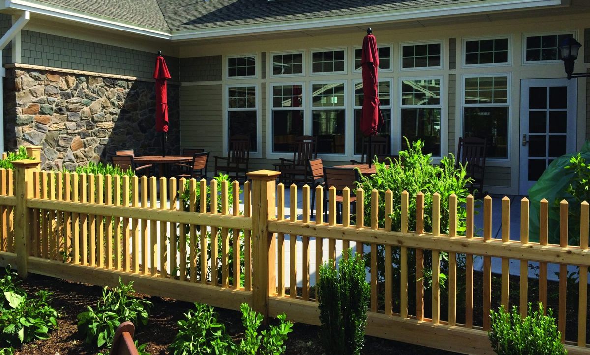 A cozy patio area with wooden fencing, outdoor seating, and red umbrellas surrounded by lush greenery.