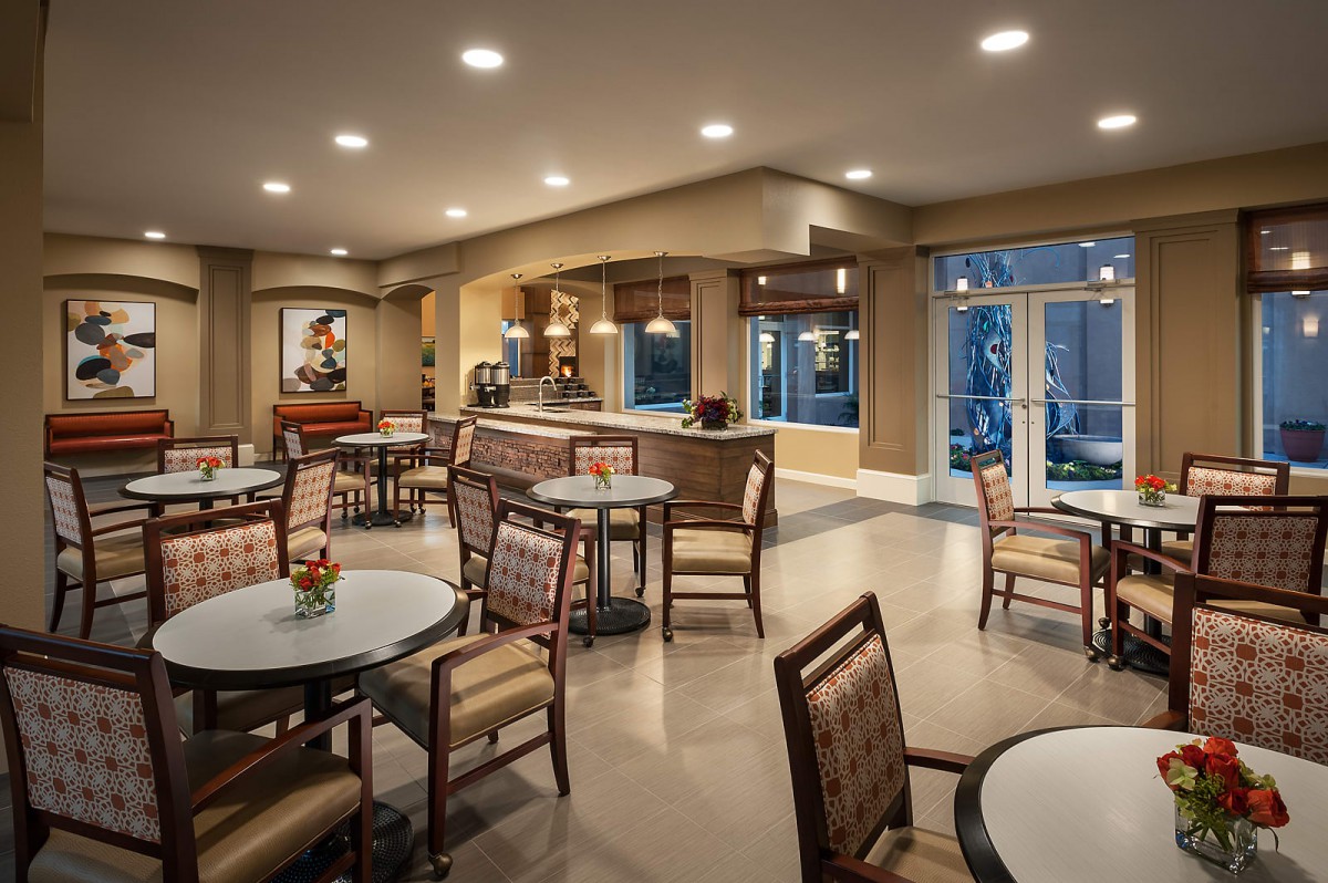 A modern dining area with neatly arranged tables and chairs, illuminated by soft overhead lighting.