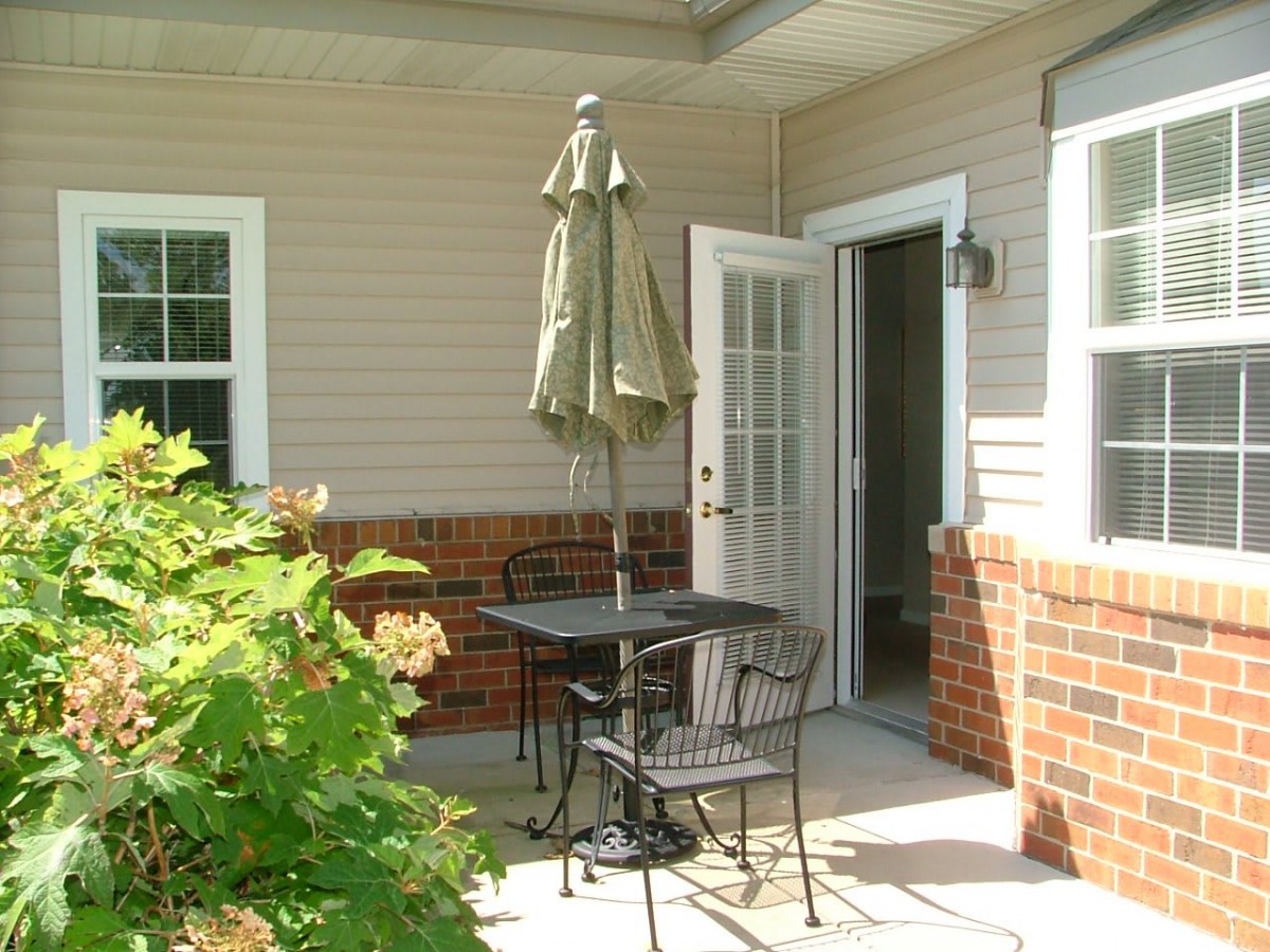A cozy outdoor patio with a table, chairs, and an umbrella by the open door of a house.
