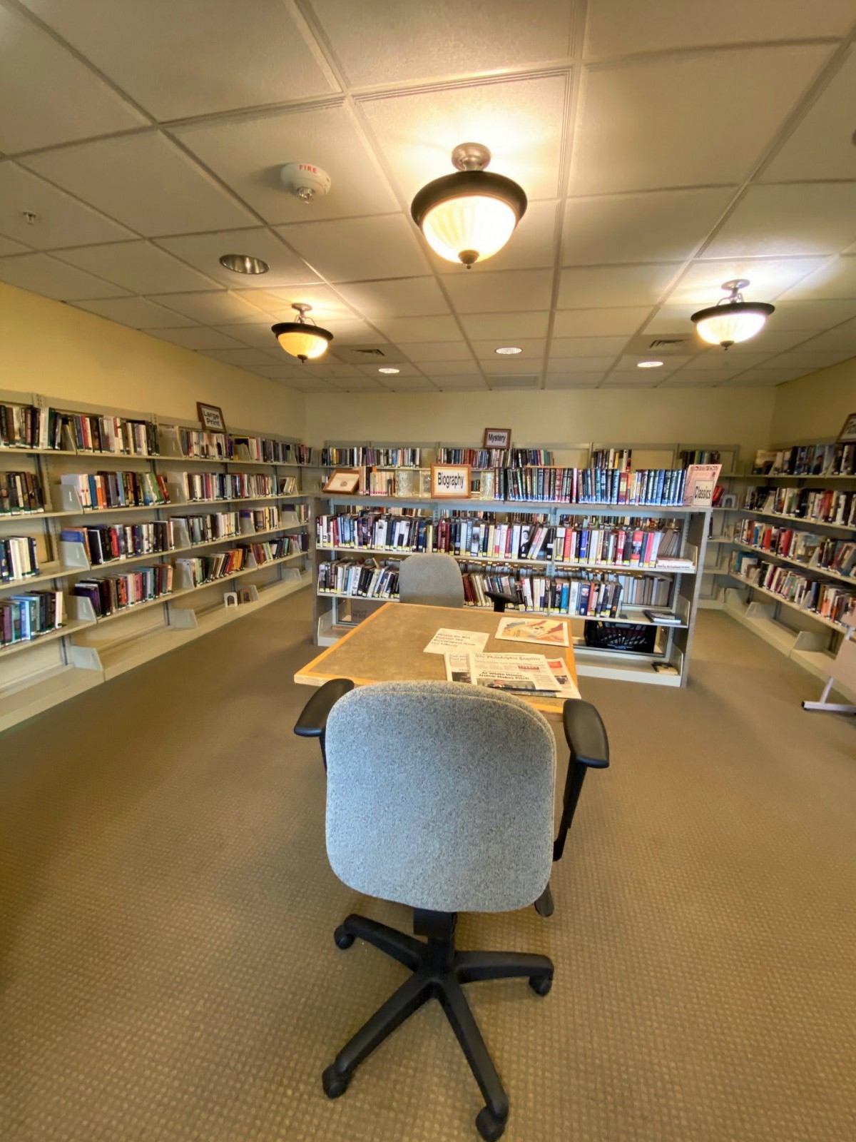 A quiet library reading room with bookshelves lined with a variety of books and a table with chairs in the center.