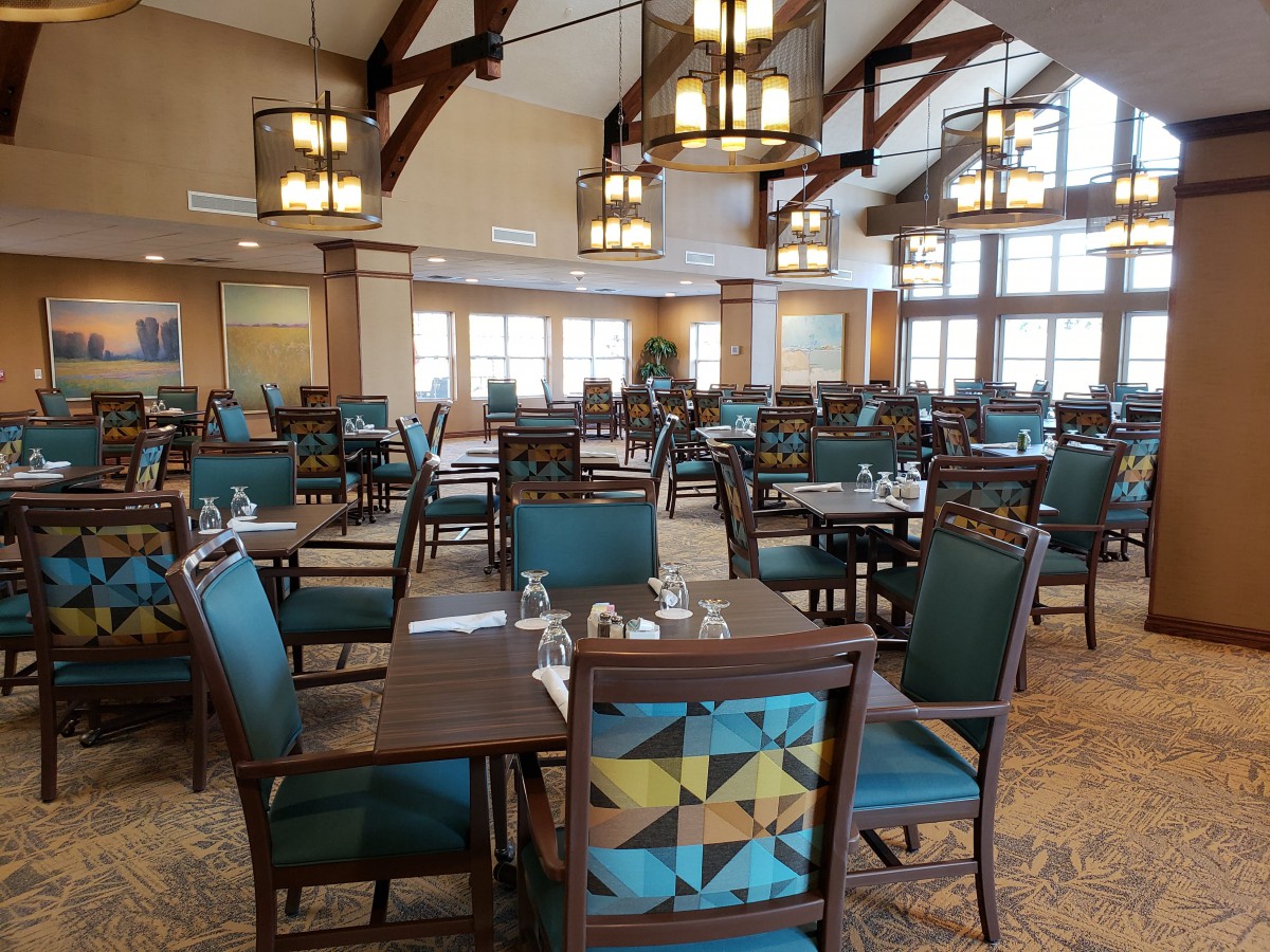 An elegant dining area with neatly arranged tables and chairs, illuminated by chandeliers in a spacious setting.