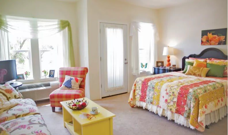 A cozy and colorful bedroom with a vibrant bedspread, a comfy chair by the window, and a small coffee table.