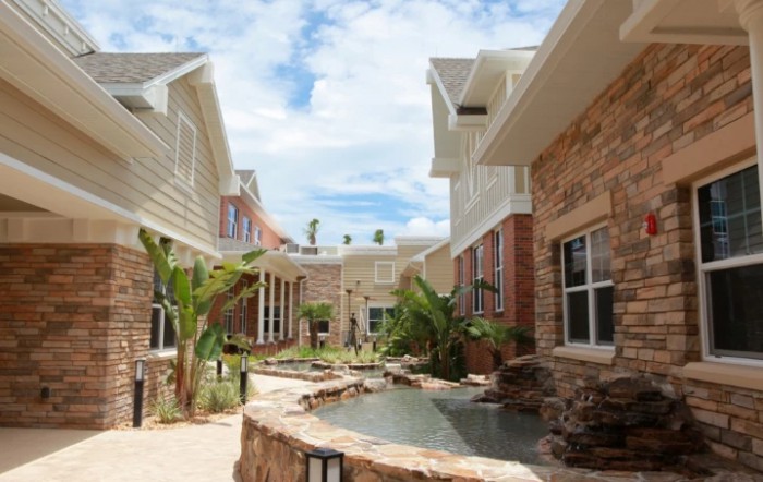 A serene courtyard between residential buildings with a stone pathway and lush greenery.