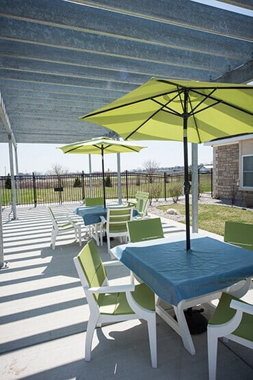 A sunny outdoor patio area with tables, chairs, and umbrellas providing shade.