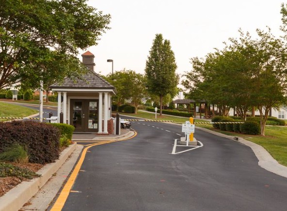 A driveway entrance with a gatehouse surrounded by trees and landscaping.