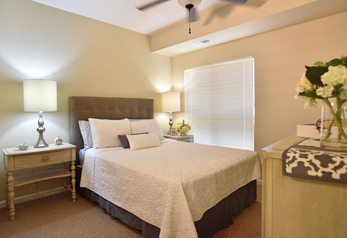 A cozy bedroom with a neatly made bed, bedside lamps, and window blinds.