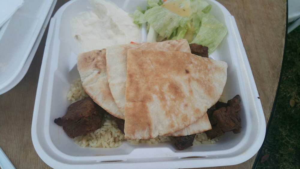 A takeout meal featuring pita bread, meat, rice, salad, and tzatziki sauce.