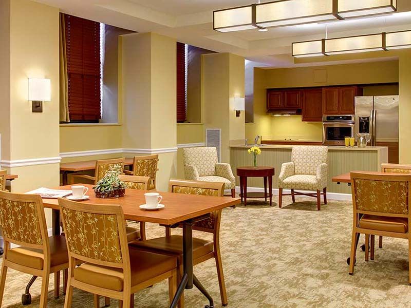 A modern dining area with wooden tables and chairs, adjacent to a kitchen space.