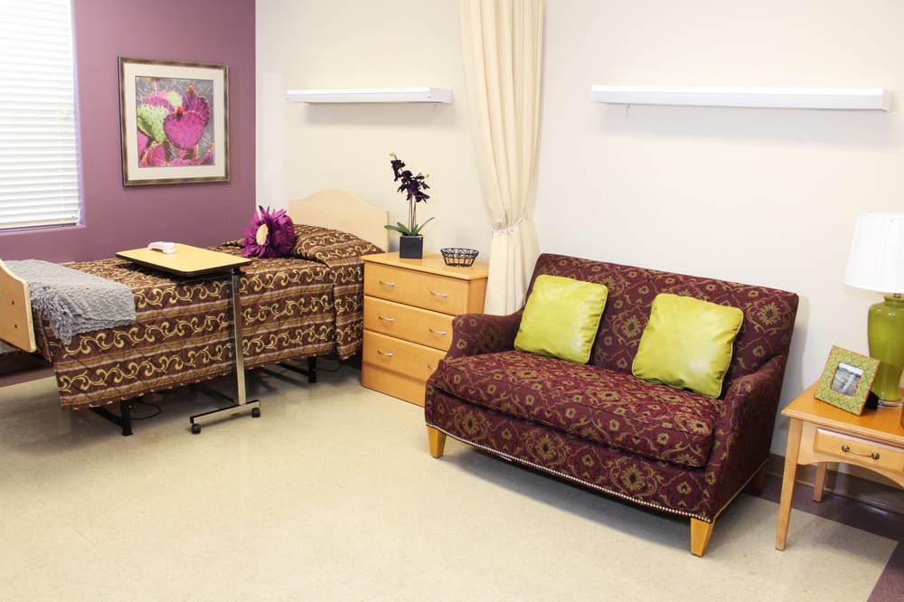 A well-furnished hospital patient room with a bed, sofa, and decorative touches.