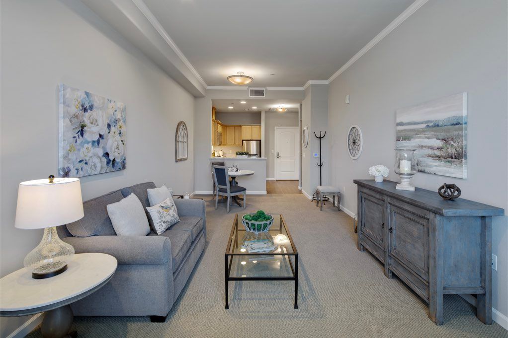 A cozy living room with a modern design featuring a gray sofa, a glass coffee table, and a dining area in the background.