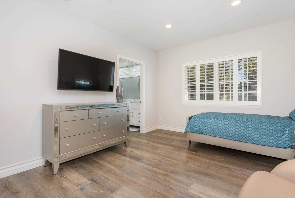 A modern minimalist bedroom with hardwood floors, a television mounted on the wall, and a dresser.