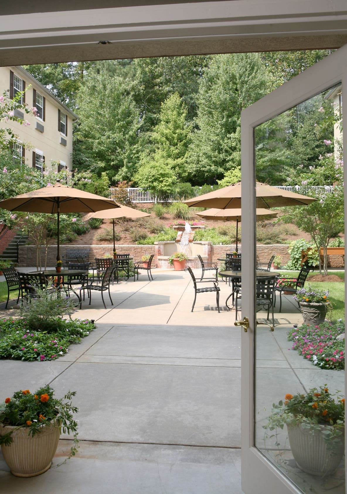 A serene patio area with tables, chairs, and umbrellas surrounded by lush greenery.