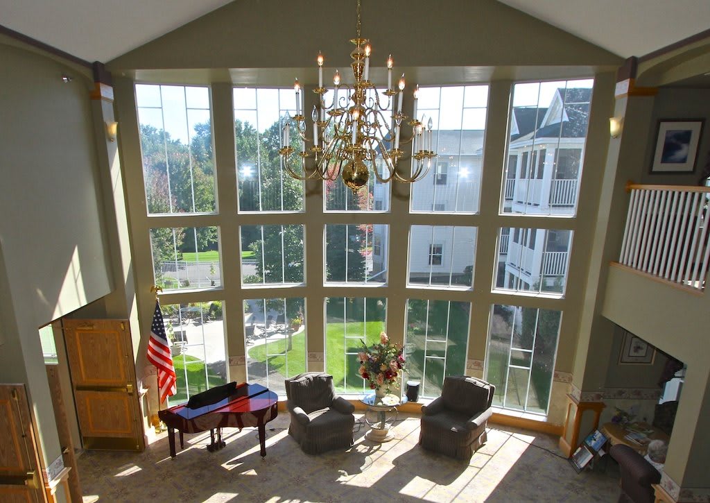 A spacious room with large windows, a chandelier, and a seating area, featuring an American flag and a piano.