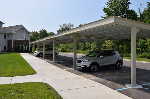 A view of a carport with two parked cars, surrounded by greenery and clear blue skies.